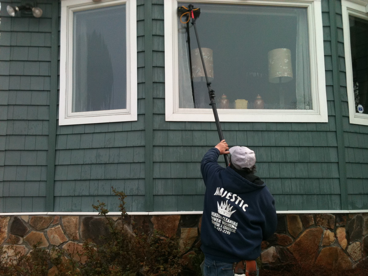 Man wearing "Majestic Window Cleaning" hoodie washing exterior of residential bay window