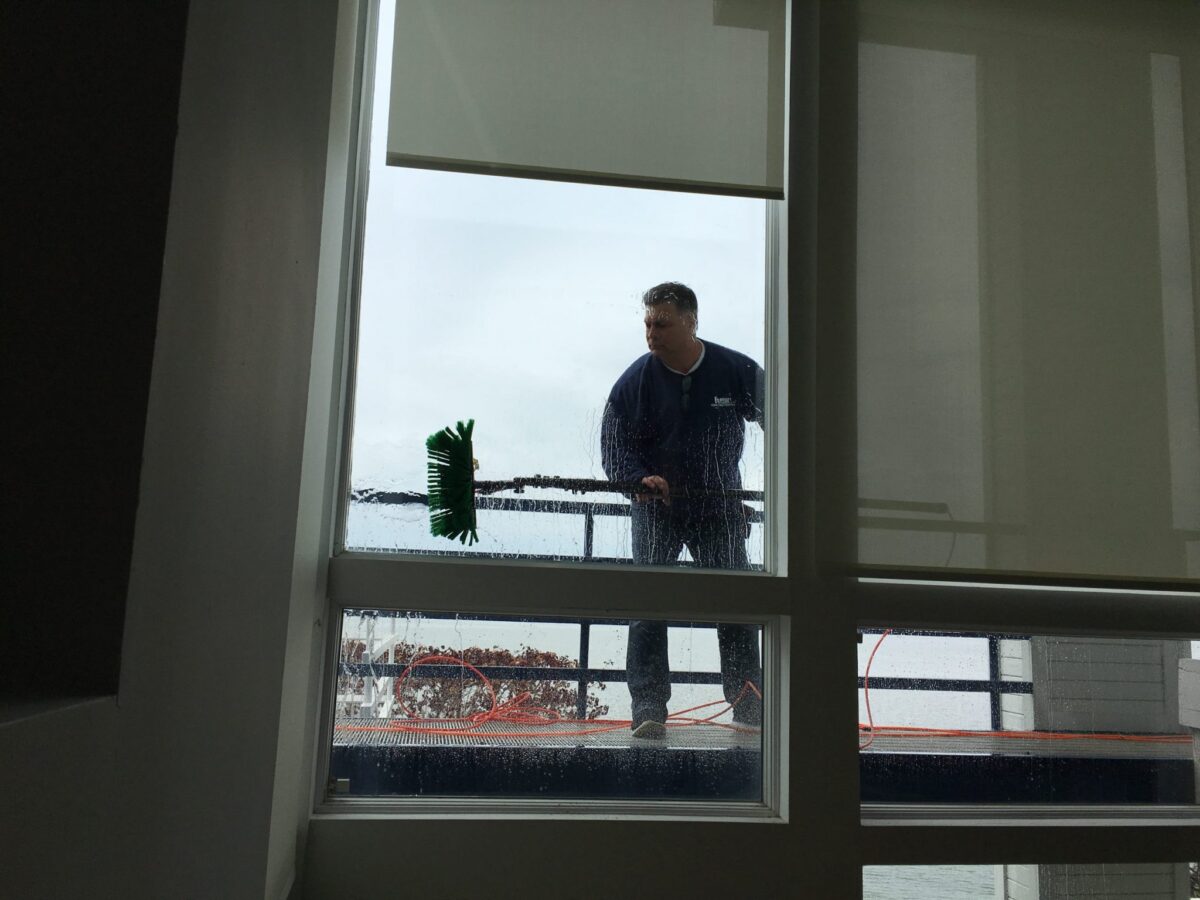Man in navy blue "Majestic Window Cleaning" shirt washing exterior surface of residential window