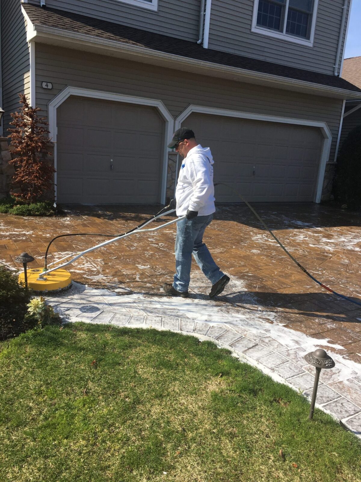 Man cleaning brick residential driveway with professional power washing equipment