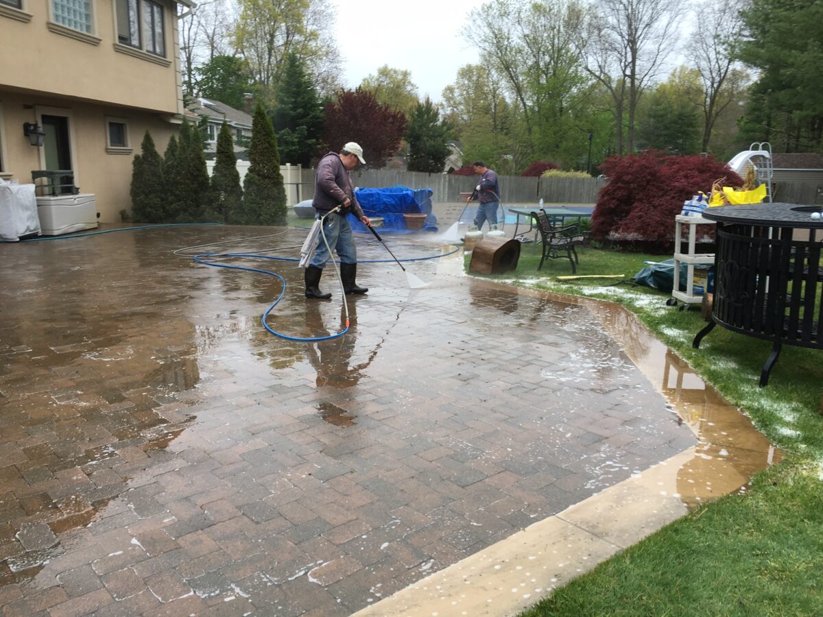 Technicians cleaning brick patio using professional pressure washing equipment