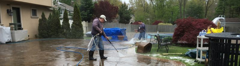 Power washing technicians cleaning concrete patio with professional pressure washing equipment