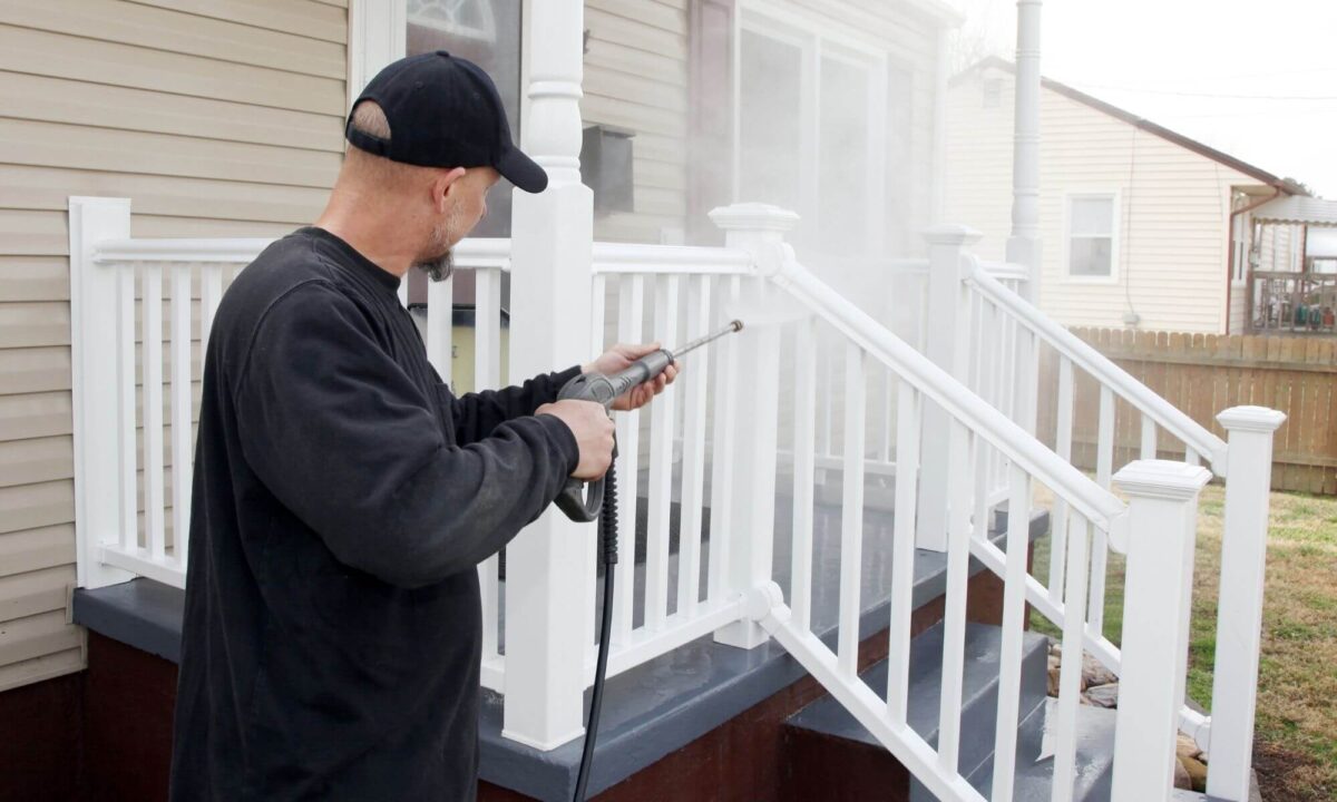 Technician power washing white railings and wooden stairs to front porch with professional equipment