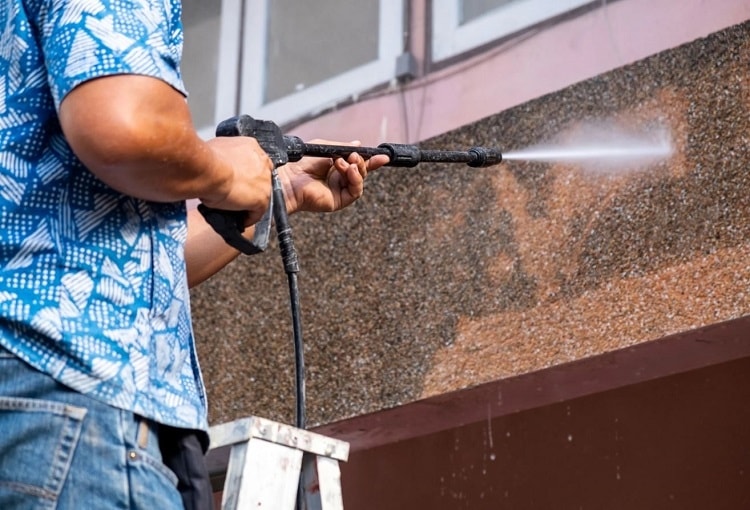 Homeowner pressure washing brick exterior of home