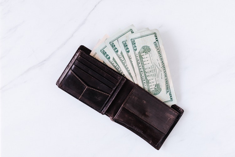 Twenty dollar bills inside brown leather wallet on white table
