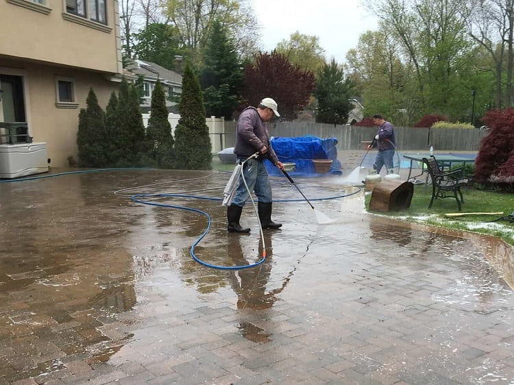 Professional power washers cleaning brick residential driveway in Long Island, New York