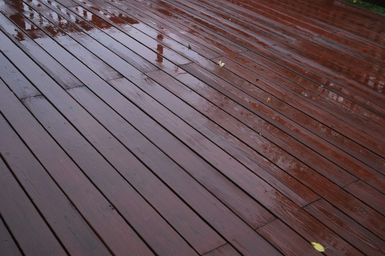 Cherry wood paneled outdoor deck freshly damp from rain with single yellow leaf on surface