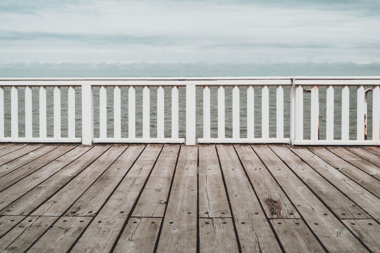 Faded wooden deck on waterfront with white wood railing