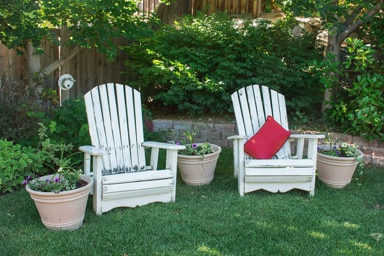 White outdoor chairs with red throw pillow beside backyard planters