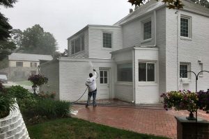 Pressure washing rain gutters of white paneled home