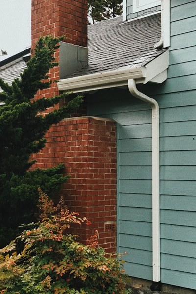 Rain gutter on side of green paneled house beside brick crimney