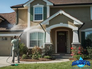Man pressure washing stucco front exterior of two-story home