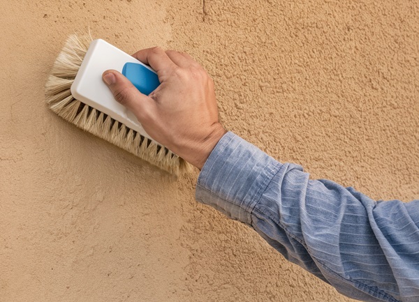 Arm scrubbing beige stucco wall with white wire cleaning brush